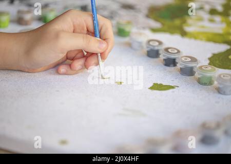 Foto sfocata ritagliata di pittura femminile a mano con pennello su carta, fuoco selettivo su vernici acriliche in scatole di plastica. Foto Stock