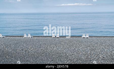 Spiaggia di ciottoli vuota con lettini bianchi in una giornata di sole. Stagcape in tempo buono. Mancanza di persone nel resort Foto Stock