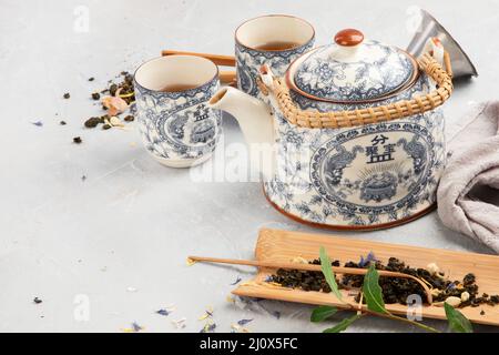 Teiera asiatica con tè alle erbe su sfondo chiaro. Foglie di piante, composizione naturale di tè a base di erbe. Foto Stock