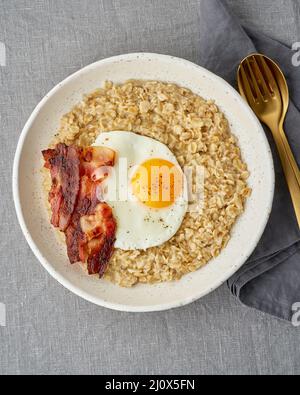 Farinata d'avena, uova fritte e pancetta fritta. Abbondante colazione a base di grassi ad alta caloria, fonte di energia. Verticale Foto Stock