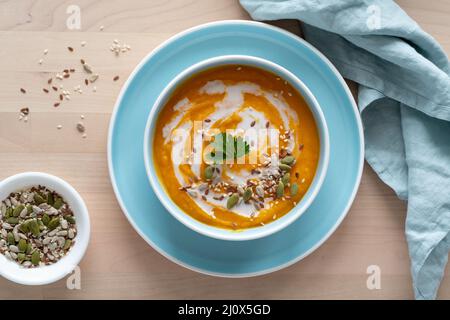 Zuppa di zucca con latte di cocco e semi in ciotola blu, vista dall'alto, spazio copia Foto Stock