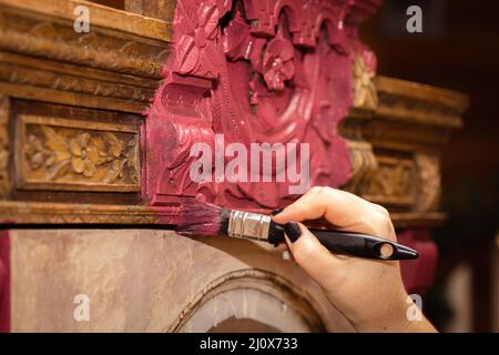 Donna mano pittura vecchio armadio shabby con ornamenti scolpiti graziosi su di esso con spazzola. Riutilizzo del vecchio. Laboratorio per il restauro di mobili antichi a. Foto Stock