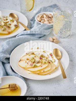 Ricotta con pere, pistacchi e sciroppo di miele o acero su piatto bianco Foto Stock