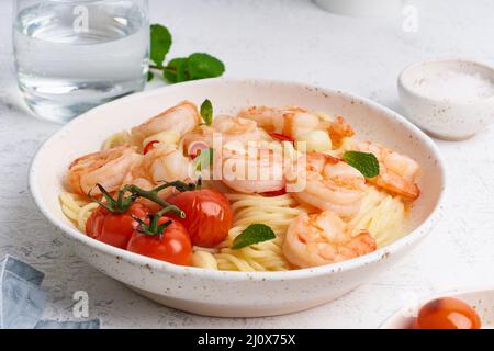 Pasta di pesce spaghetti con gamberi fritti, salsa di bechamel, foglia di menta e pomodori su tavola bianca Foto Stock