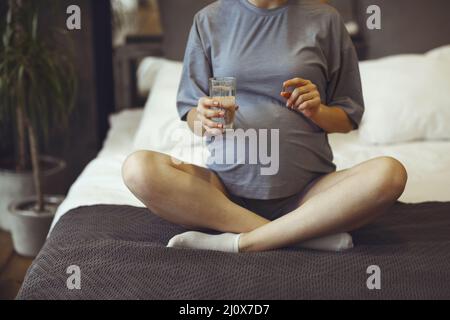 Donna incinta che prende le vitamine prenatali durante la gravidanza, tenendo il vetro dell'acqua e la pillola nelle sue mani Foto Stock