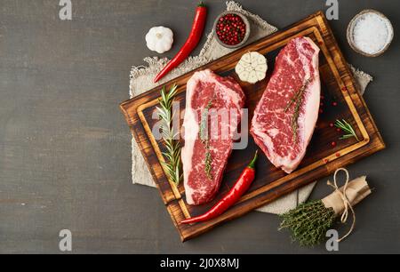 Condire la bistecca cruda con sale, timo, aglio. Due grandi pezzi interi di carne di manzo cruda Foto Stock