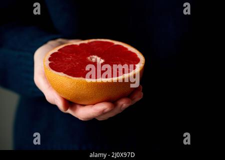 Primo piano della mano della donna che tiene fresco metà rosso brillante agrumi pompelmo di frutta Foto Stock