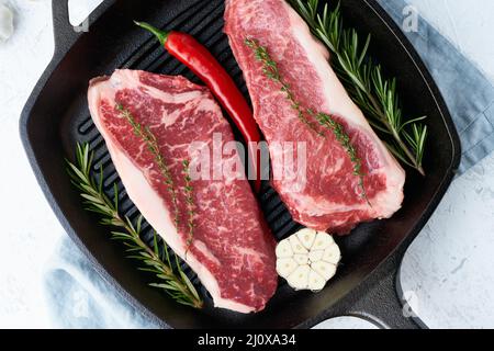 Due pezzi interi grezzi freschi, filetto di manzo, striploin di marmo in grande padella di ghisa. Foto Stock