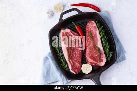 Due pezzi freschi di carne cruda, filetto di manzo, striploin di marmo in una grande padella di ghisa. Vista dall'alto Foto Stock