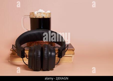 Le cuffie si trovano accanto alla tazza di caffè con marshmallows, pila di vecchi libri Foto Stock