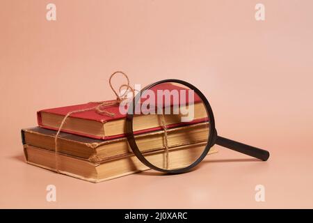 Una pila di vecchi libri martoriati legati con una corda di iuta e una lente d'ingrandimento Foto Stock