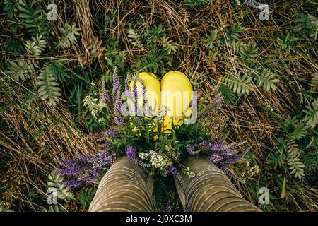 Stivali gialli in gomma con bouquet di fiori selvatici. Vista dall'alto. Foto Stock