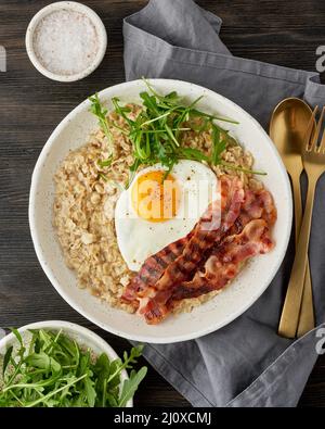 Farinata d'avena, uova fritte, pancetta fritta. Equilibrio di proteine, grassi, carboidrati. Cibo equilibrato. Verticale Foto Stock