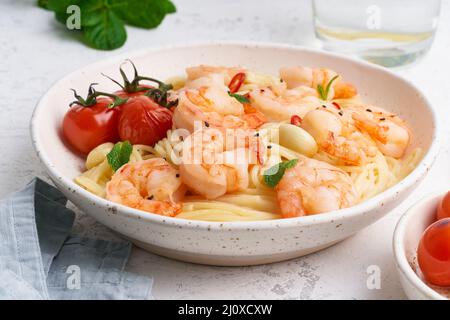 Pasta di pesce spaghetti con gamberi fritti, salsa di bechamel, foglia di menta e pomodori su tavola bianca Foto Stock