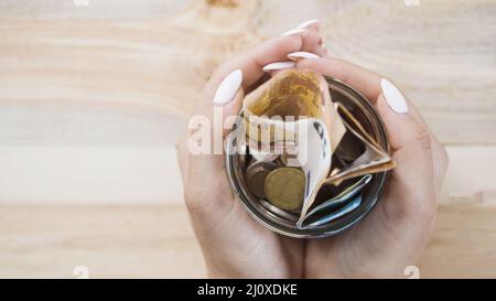 Donna tenuta a mano vaso di vetro con monete in euro sfondo di legno Foto Stock