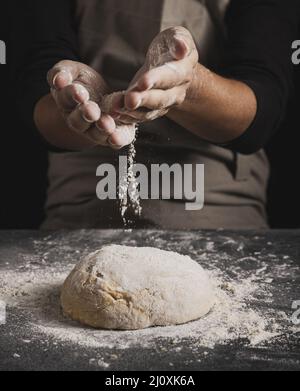 Chiudere le mani del panettiere spandendo la farina. Concetto di foto di alta qualità Foto Stock