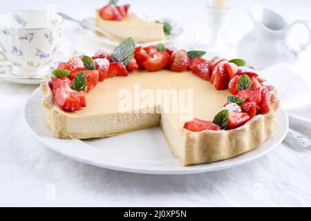 Cheesecake tradizionale tedesca con frutta alla fragola servita da vicino su un piatto di design classico con tovaglia Foto Stock