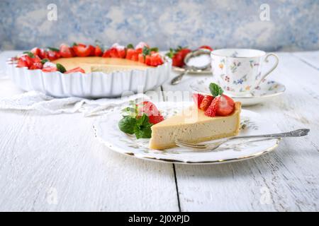 Cheesecake tradizionale tedesca con frutta alle fragole servita da vicino su un piatto di design classico su un tavolo di legno Foto Stock