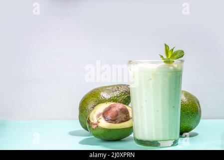 Snack drink verde sano. Vegan non latticini, keto dieta cocktail. Un bicchiere con smoothie o shake al latte di avocado e avocado fresco su tavola turchese Foto Stock