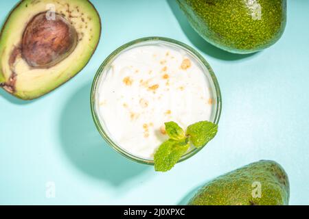 Snack drink verde sano. Vegan non latticini, keto dieta cocktail. Un bicchiere con smoothie o shake al latte di avocado e avocado fresco su tavola turchese Foto Stock