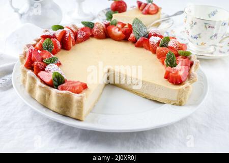 Cheesecake tradizionale tedesca con frutta alla fragola servita da vicino su un piatto di design classico con tovaglia Foto Stock