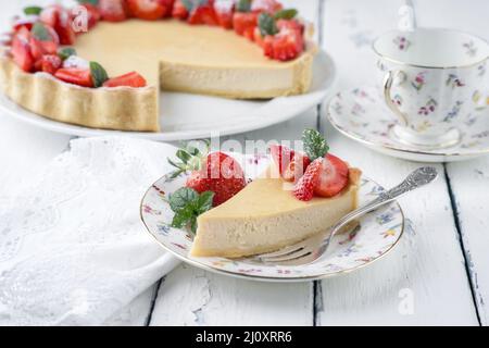 Cheesecake tradizionale tedesca con frutta alla fragola servita da vicino su un piatto di design classico con tovaglia Foto Stock