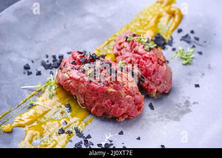 Tartaro gourmet crudo di stile moderno da filetto di manzo con salsa di senape e capperi serviti da vicino su un piatto di design Foto Stock