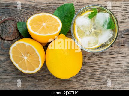 Limonata in un bicchiere, mezzo limone, foglie fresche su un vecchio tavolo di legno. Una rinfrescante bevanda fredda d'acqua con ghiaccio, menta e fette Foto Stock