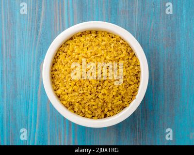 Ciotola bianco con materie di bulgur sul blu sullo sfondo di legno. Vista dall'alto. Foto Stock
