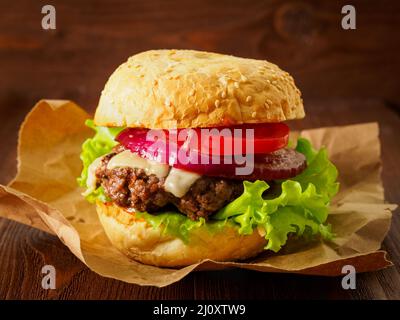 Grande e delizioso hamburger fatto in casa con cotoletta di manzo, formaggio, cipolla, pomodoro e lattuga su panini tostati. Fast food americano, malessere Foto Stock