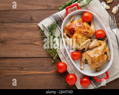 Due carcasse di pollo fritto in una ciotola, mandrini cotti al forno con pomodori, con crosta croccante, su linguetta rustica di legno marrone scuro Foto Stock