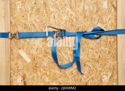 Cricchetto per camion, fascette fermacavo, scatola truciolare. Nastro di carico blu sulla superficie in legno osb Foto Stock