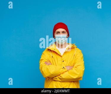 Ritratto di uomo in maschera medica protettiva si alza con le braccia incrociate e guarda la macchina fotografica Foto Stock