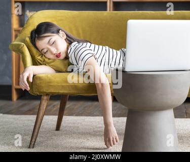 La giovane ragazza asiatica si addormentò sul divano davanti a un laptop. Cute annoiata donna che guarda il film noioso Foto Stock