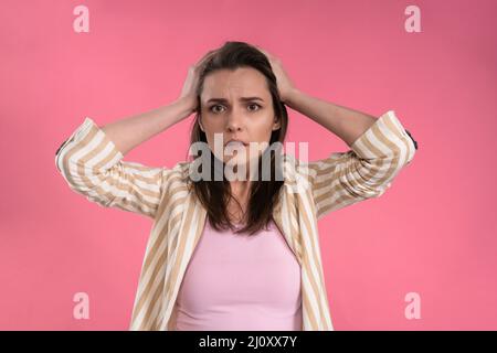 Stressed or having a headache businesswoman in suit holding her head with eyes shut isolated on pink background. Stressed employ Stock Photo