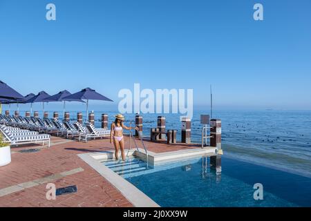 Donna di fronte alla piscina Infinity che si affaccia sull'oceano di Città del Capo Sud Africa, uomo e donna in piscina durante il sole Foto Stock