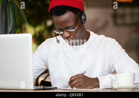 Concentramento nero hipster maschio in cuffie, occhiali stoiding o lavorare da remoto sul computer Foto Stock