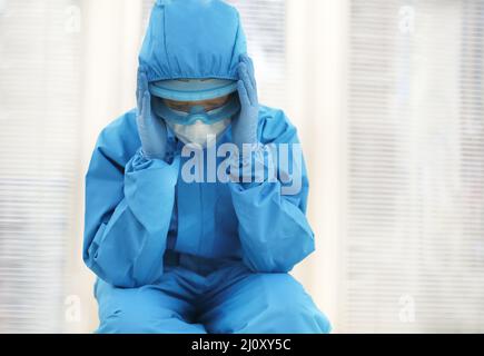 Tired depressed nurse in personal protective equipment PPE after difficult shift during Covid-19. Stock Photo