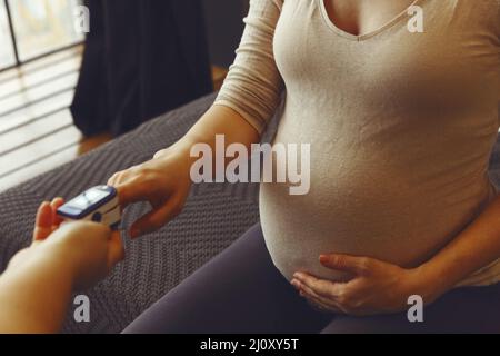 Medico che misura il livello di saturazione di ossigeno di una donna in gravidanza con pulsossimetro durante la visita a casa Foto Stock