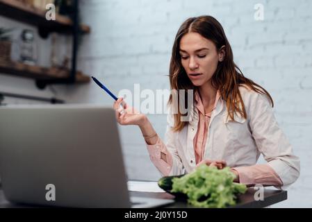 Giovane medico nutrizionista femminile che lavora dalla sua scrivania di fronte al suo laptop. Foto Stock