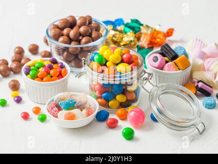 Caramelle al cioccolato al latte in guscio con gomme da zucchero gelate e liquirizia e caramelle di sherbet di frutta su sfondo bianco. Con marshmallow e stra Foto Stock