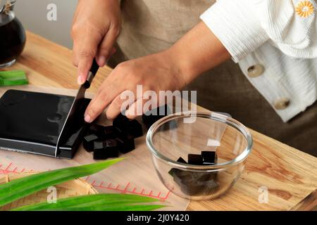 Asian femmina taglio incau Hitam o Black Grass Jelly Pudding in pezzi, cibo sano Foto Stock