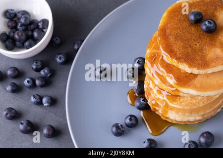 Vista ad angolo alto delle frittelle accatastate con bacche blu e sciroppo nel piatto sul tavolo Foto Stock