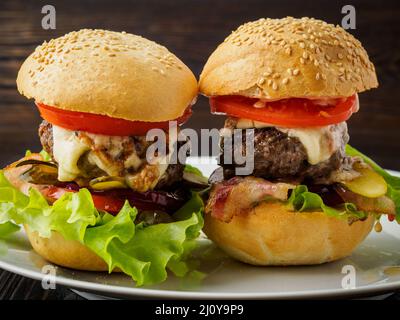 Due deliziosi hamburger fatti in casa con cotoletta di manzo, formaggio, cipolla, pomodoro e lattuga sui panini tostati. Fast food americano, unhe Foto Stock