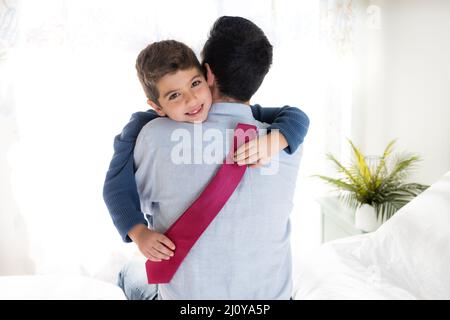 Figlio che abbracciava il padre con una cravatta sulle mani Foto Stock