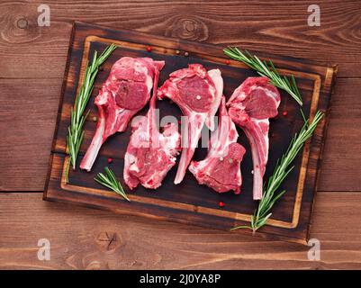 Cotolette di agnello crudo su osso su sfondo di legno marrone scuro, costolette di agnello, vista dall'alto. Foto Stock