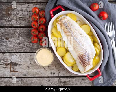 Merluzzo di pesce cotto al forno con patate. Vecchio legno scuro sfondo rustico grigio, vista dall'alto, spazio copia Foto Stock