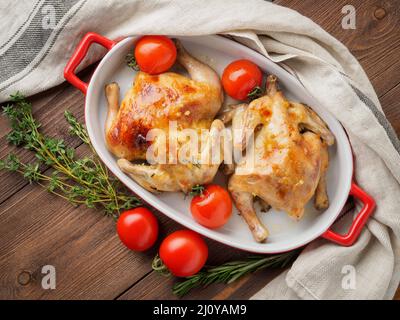Due carcasse di pollo fritto in una ciotola, mandrini cotti al forno con pomodori, con crosta croccante, su legno marrone scuro rustico ta Foto Stock