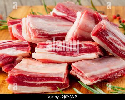 Piccoli pezzi di costolette di agnello crude su tagliere di legno su vecchio sfondo rustico di legno, vista laterale Foto Stock