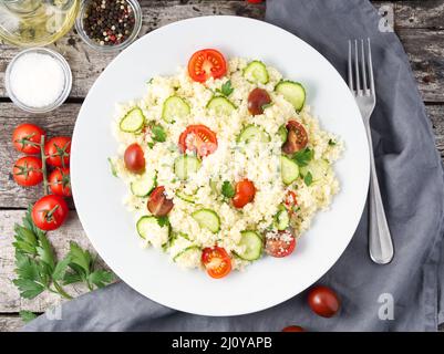 Insalata di verdure fresche con couscous, pomodori, cetrioli, prezzemolo, tavola rustica di legno scuro, vista dall'alto Foto Stock